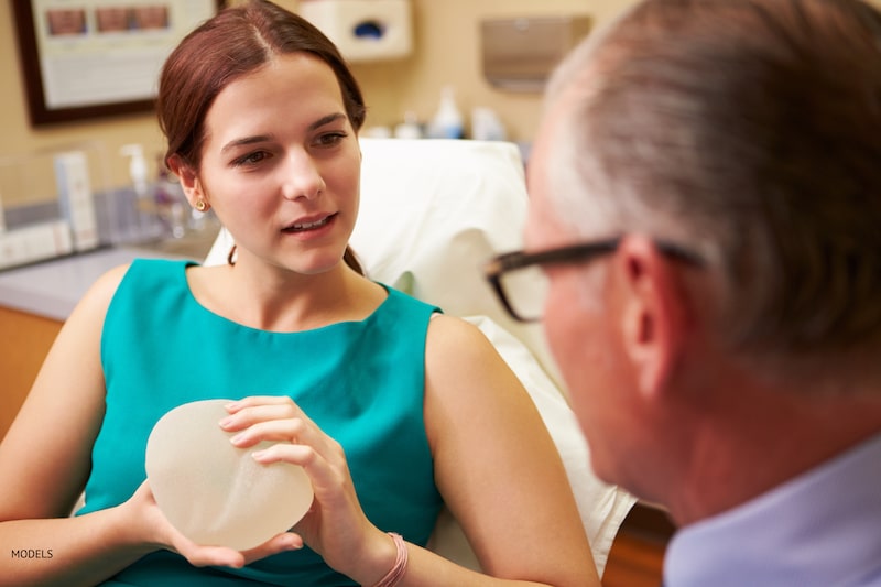 Woman holding a breast implant during a consultation with her plastic surgeon.